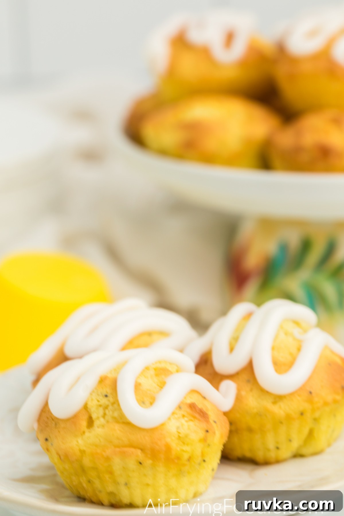 Zesty Air Fryer Lemon Poppy Seed Muffins 2 Lemon Poppy Seed Muffins with lemon glaze on a plate, ready to serve.
