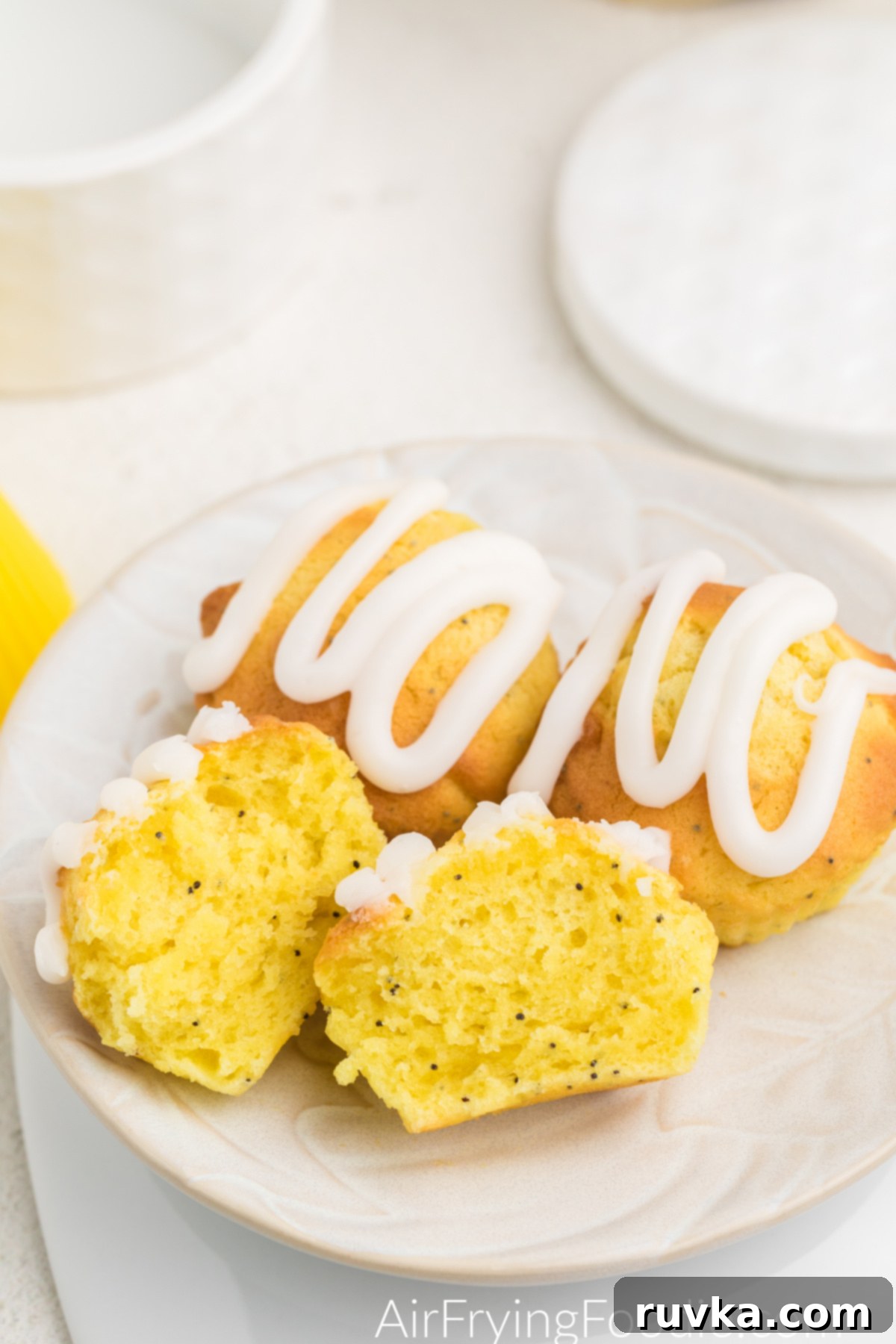 Zesty Air Fryer Lemon Poppy Seed Muffins 8 Lemon Poppy Seed Muffin sliced in half on a plate with other lemon poppy seed muffins.