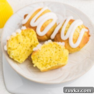 Zesty Air Fryer Lemon Poppy Seed Muffins 10 Lemon poppy seed muffins topped with lemon glaze, on a plate, with one muffin sliced in half.