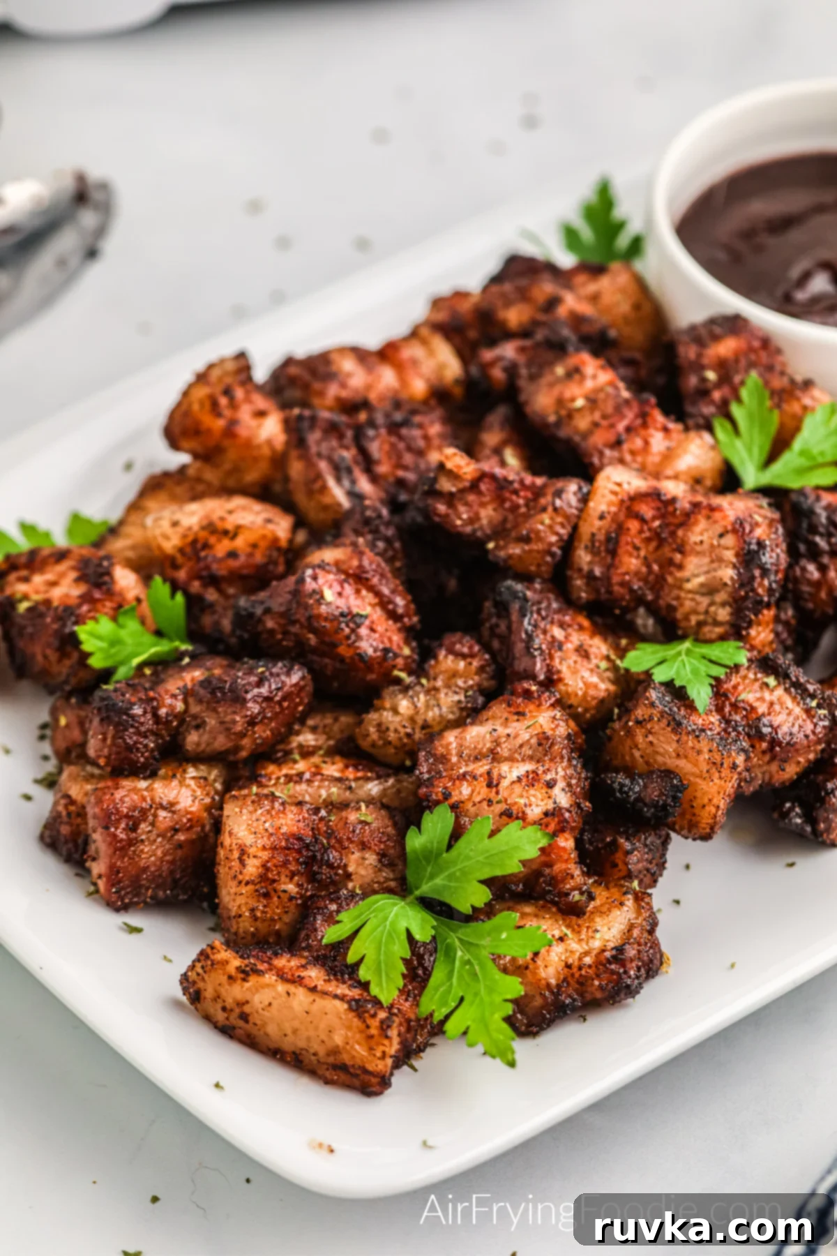 Air Fried Pork Belly Perfection 2 Air fryer pork belly bites in a plate with fresh parsley and BBQ dipping sauce.