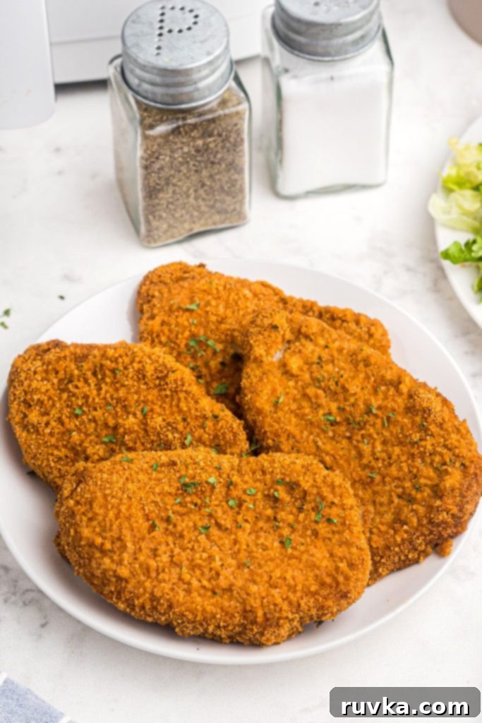 Crispy Air Fryer Pork Chops 8 Golden crispy pork chops on a white plate after being cooked in the air fryer