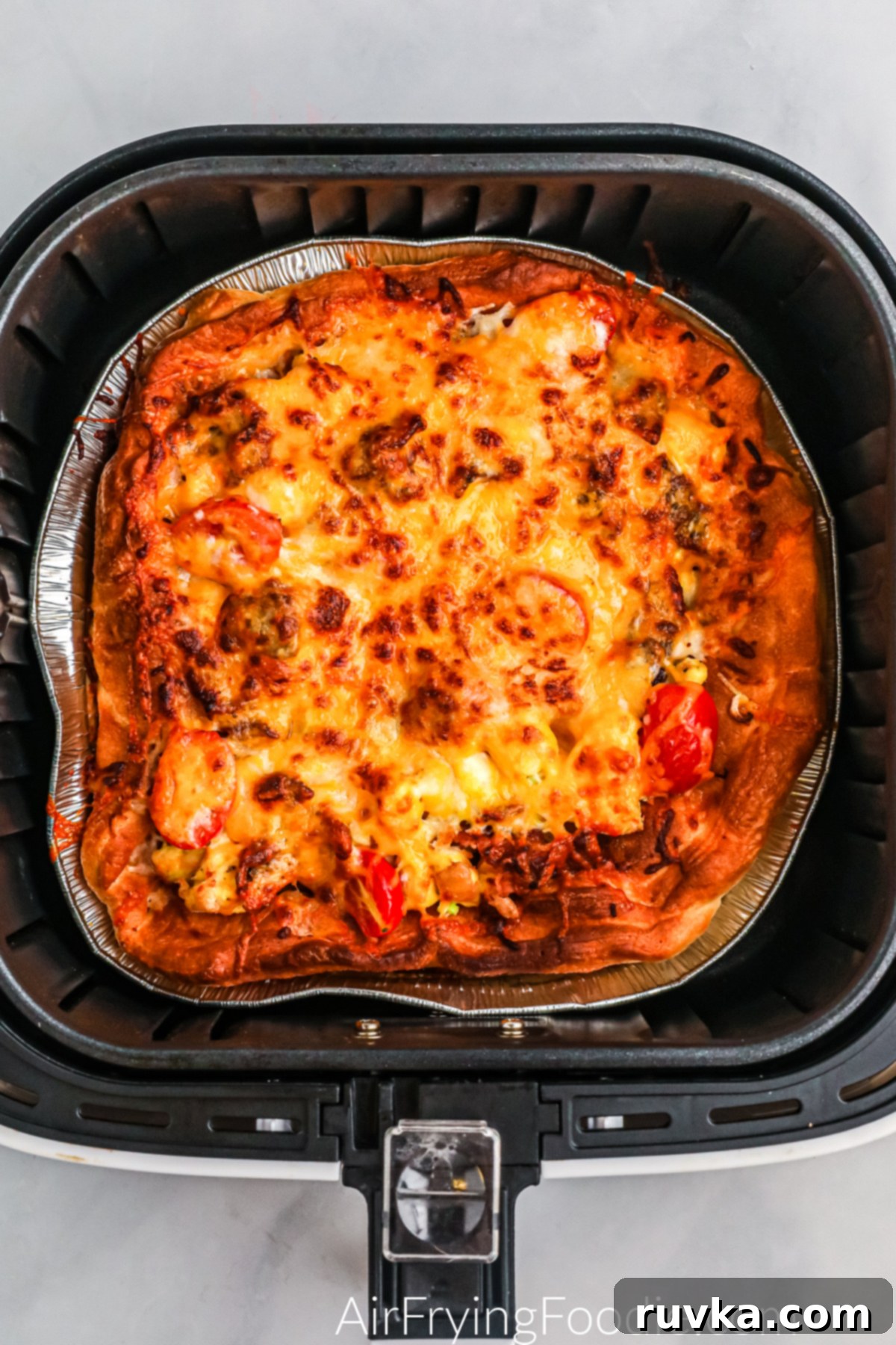 Crispy Air Fryer Breakfast Pizza 5 Breakfast pizza in the basket of the air fryer topped with cheese and ready to serve.