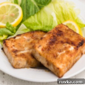 Perfect Air Fryer Frozen Salmon 9 Perfectly cooked air fryer frozen salmon, served on a white plate with a fresh side salad and a lemon slice.
