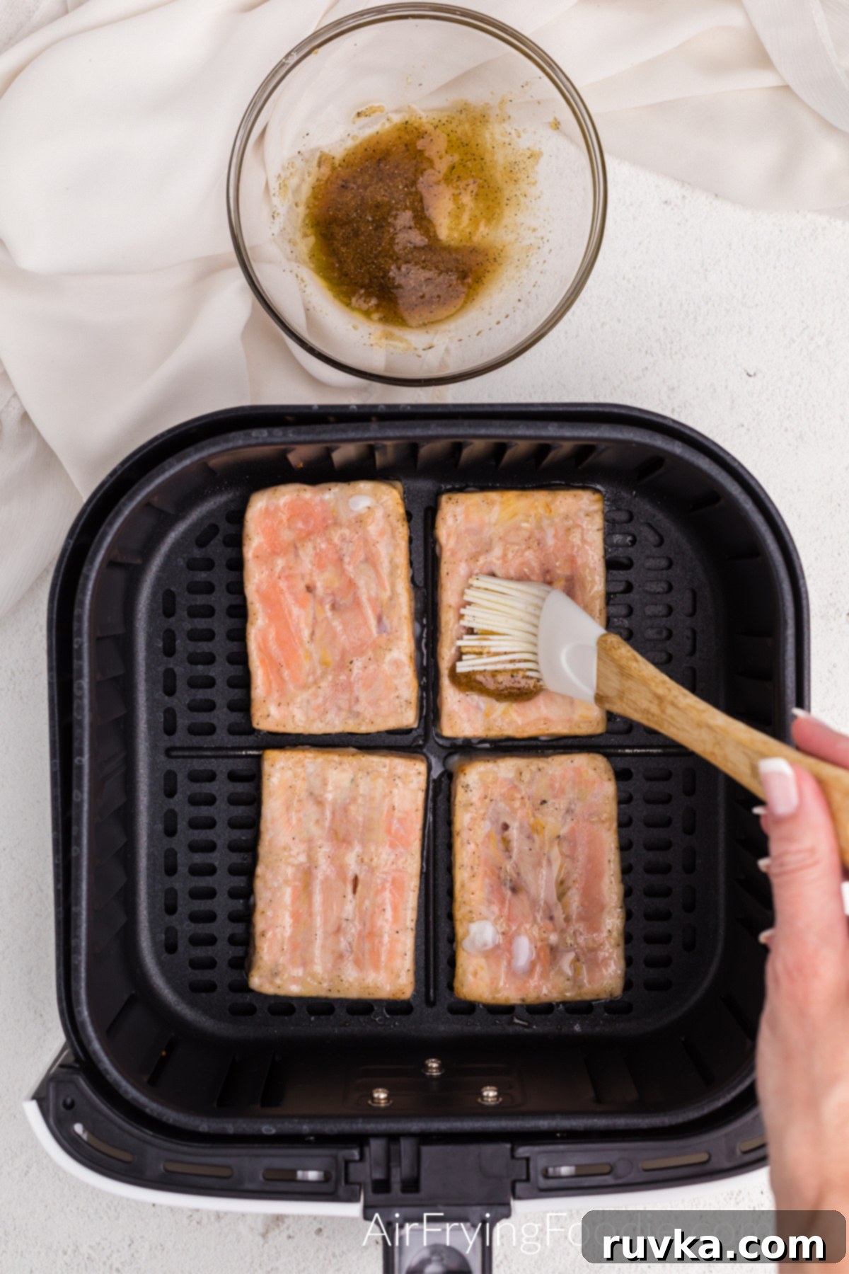 Perfect Air Fryer Frozen Salmon 5 Defrosted salmon in the air fryer basket being brushed with a homemade sweet and savory marinade before the final cooking stage.