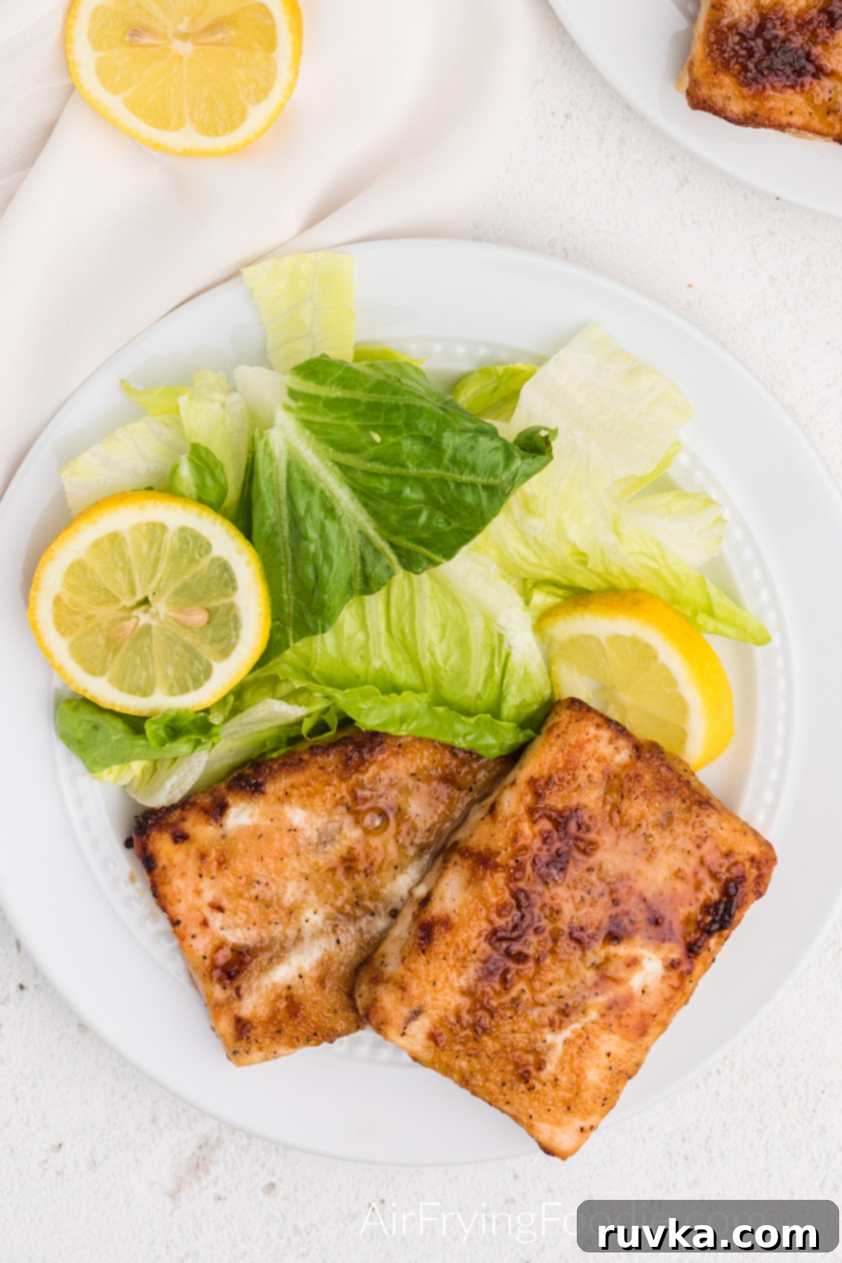 Perfect Air Fryer Frozen Salmon 7 A vibrant plate of fully cooked air fryer frozen salmon, beautifully seasoned, served alongside a fresh green salad and lemon slices.