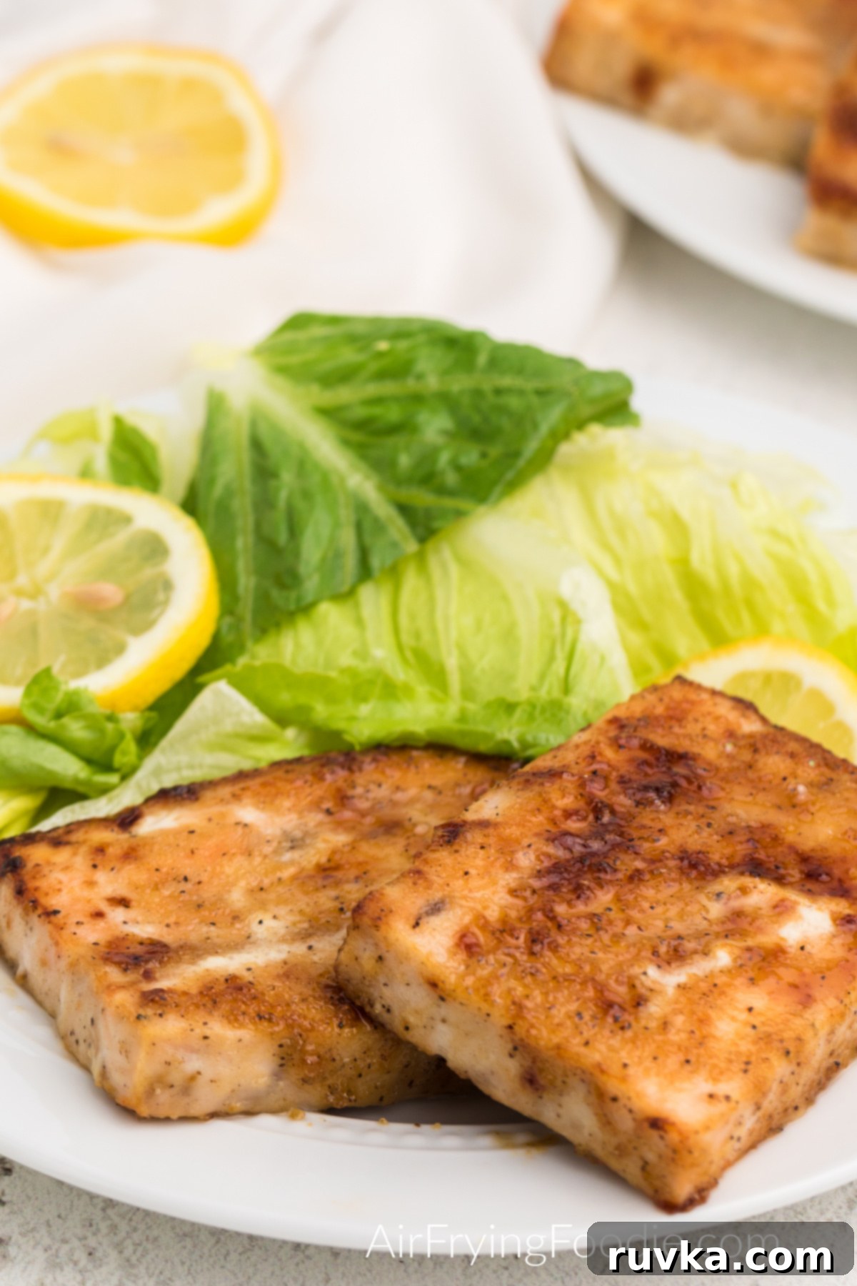 Perfect Air Fryer Frozen Salmon 8 A beautifully seasoned and perfectly cooked air fryer frozen salmon fillet, presented on a white plate with a side salad and fresh lemon slices.
