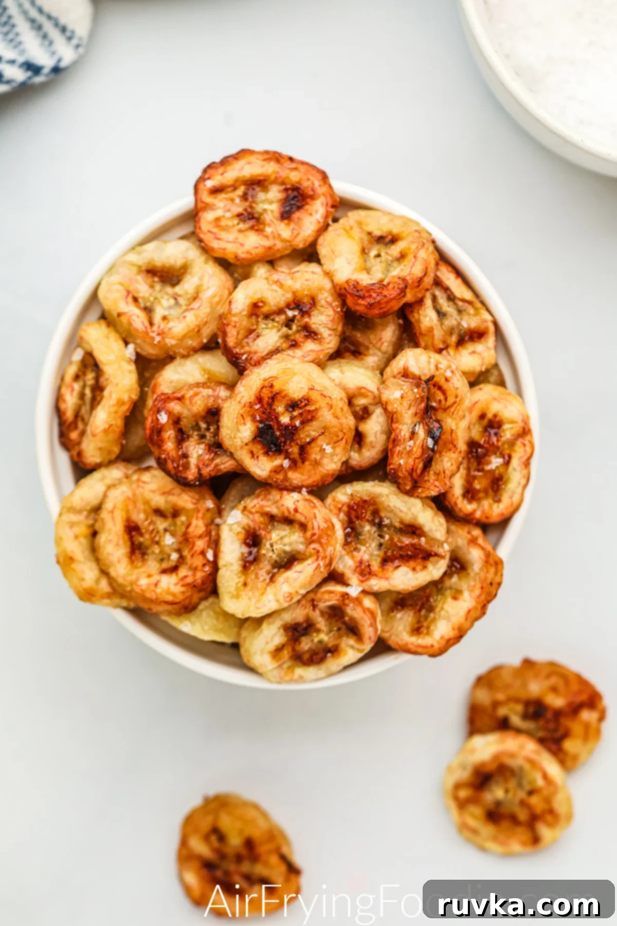 Crispy Air Fryer Banana Chips 2 Air fried banana chips in a bowl with salt sprinkled on them, ready to serve.