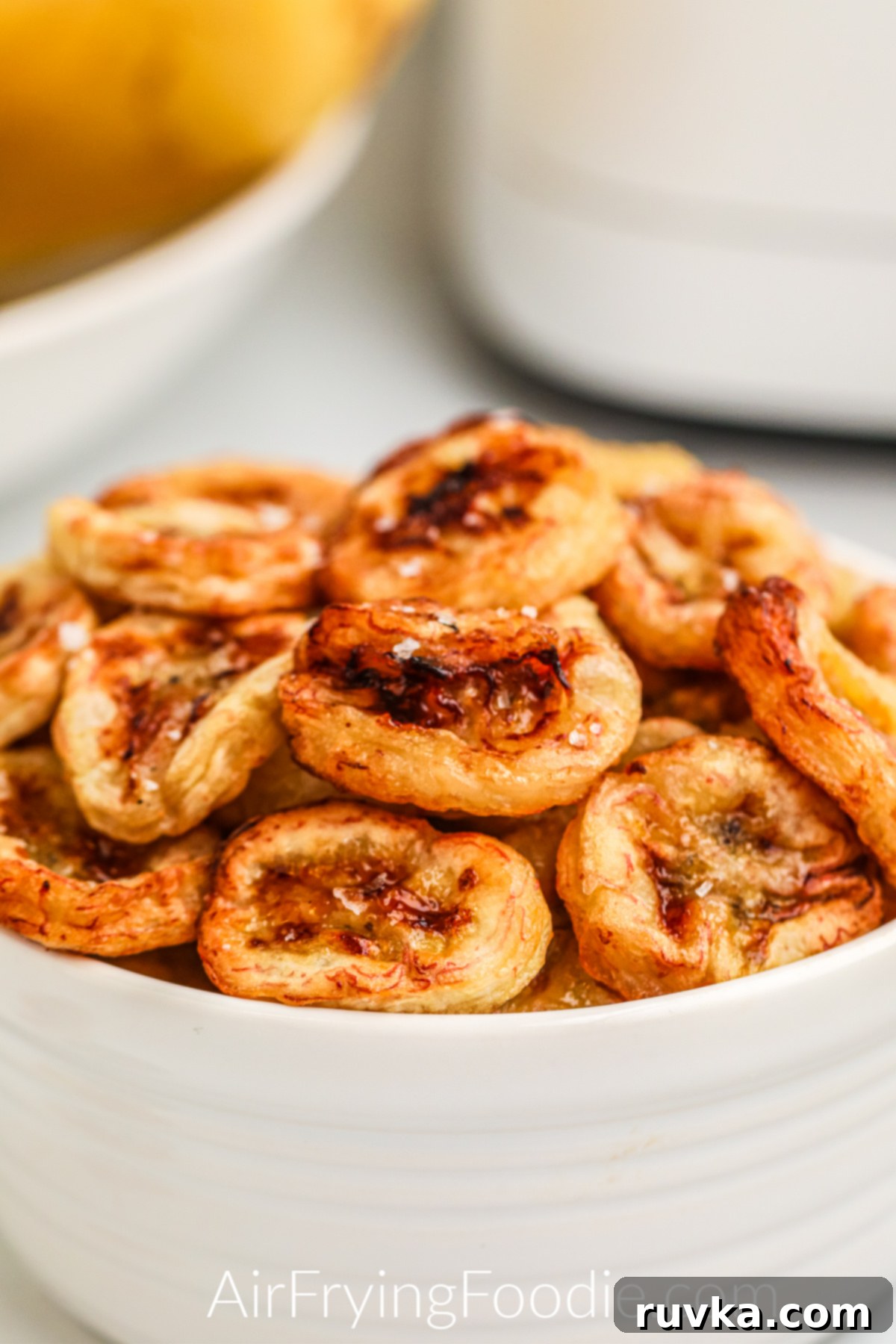 Crispy Air Fryer Banana Chips 9 Close up shot of banana chips made in the air fryer, and then placed in a white bowl and topped with kosher salt before serving.
