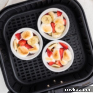 Delicious Air Fryer Strawberry Banana Bowl 9 Strawberry Banana Bowls with melted marshmallows and chocolate drizzle in the basket of the air fryer.