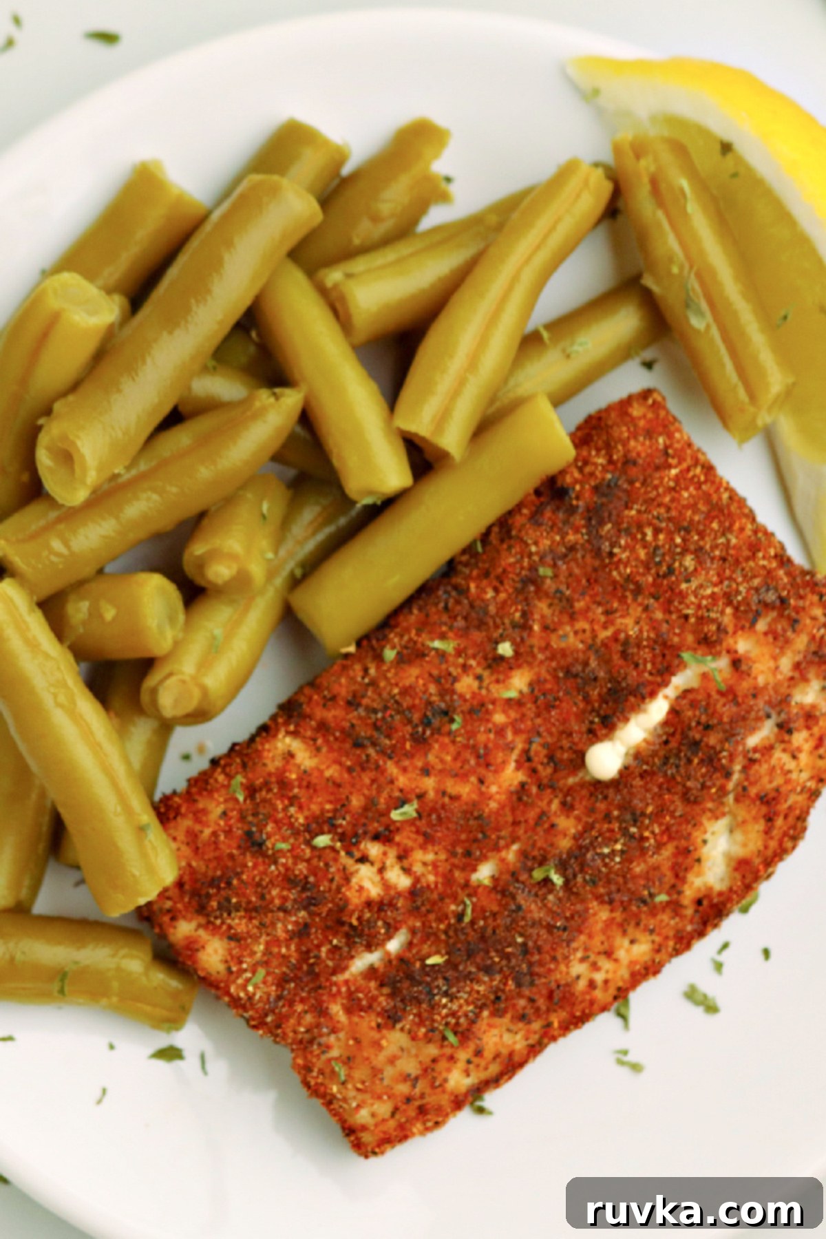 Quick and Delicious Air Fryer Mahi Mahi 3 Overhead shot of mahi mahi on a plate with green beans and a lemon slice.