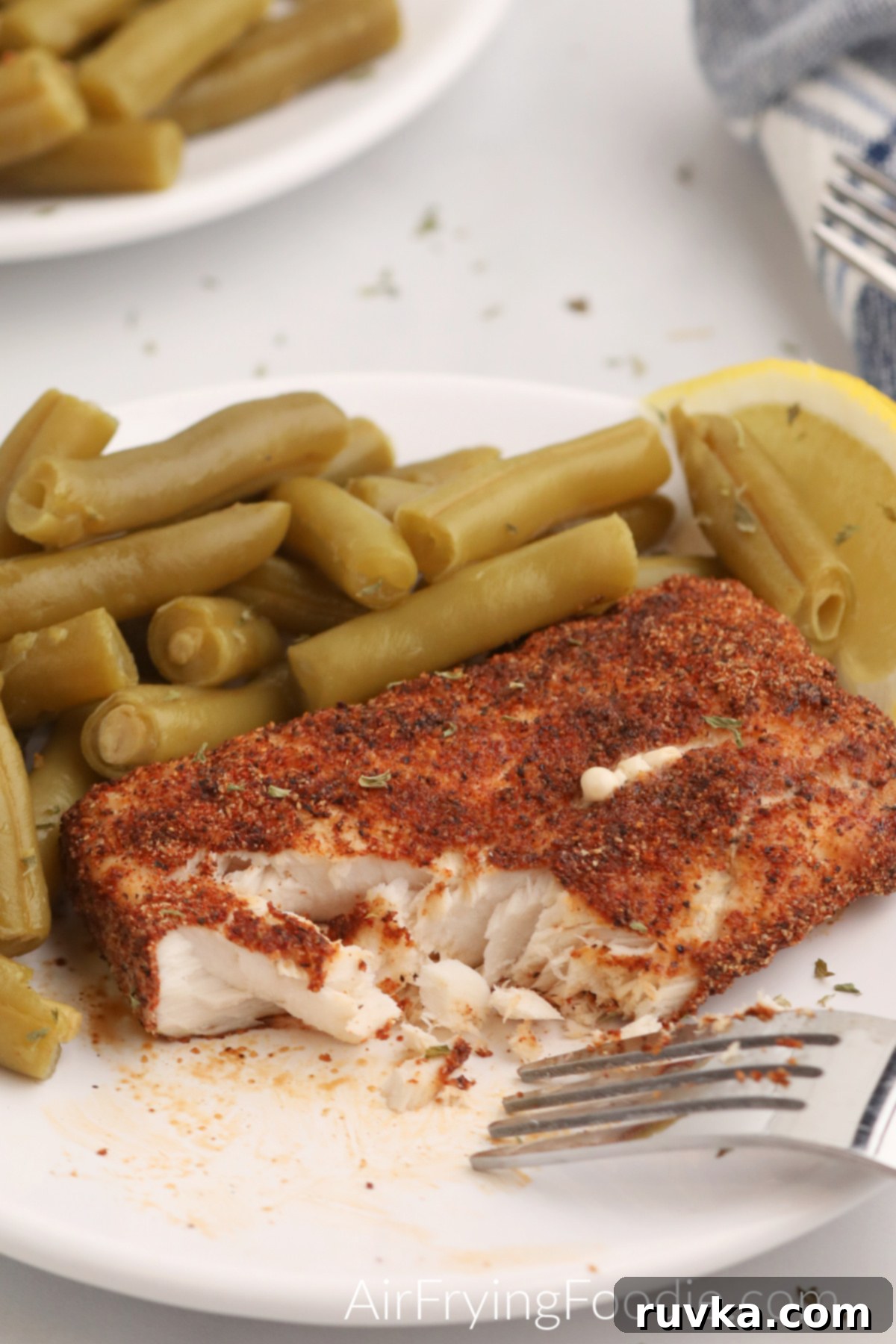 Quick and Delicious Air Fryer Mahi Mahi 4 Close up of Mahi Mahi on a white plate with green beans and a lemon slice.