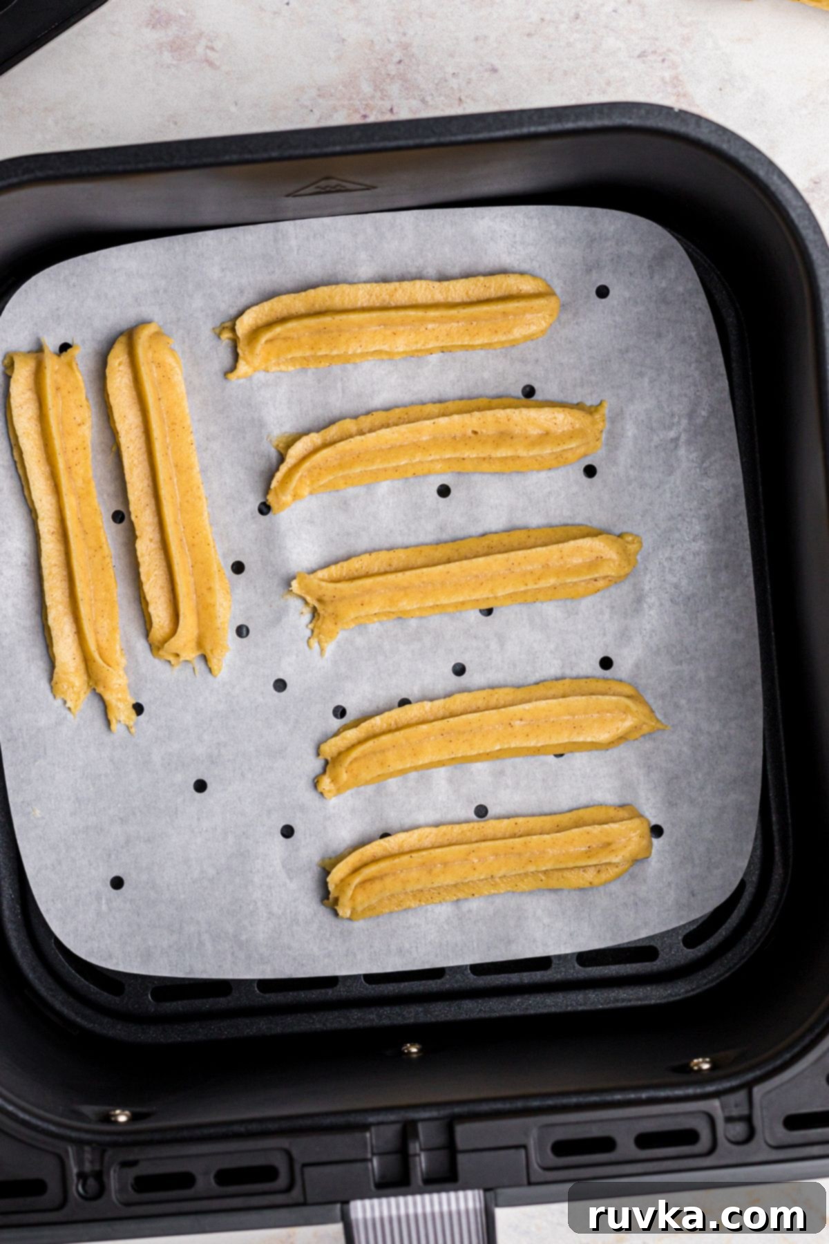 Crispy Air Fryer Churros 7 Air fryer churro dough on parchment paper in the air fryer basket.