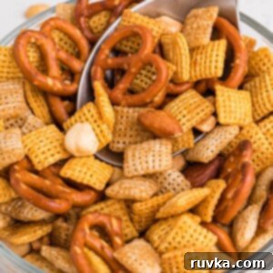 Easy Air Fryer Chex Mix 10 Clear bowl filled with chex mix on a white table with spoon scooping some out