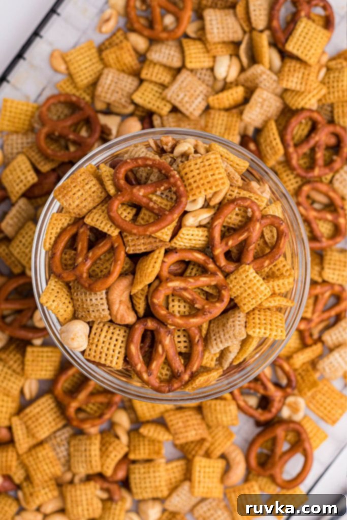 Easy Air Fryer Chex Mix 9 Clear glass bowl filled with Chex mix and more mix scattered around the table.