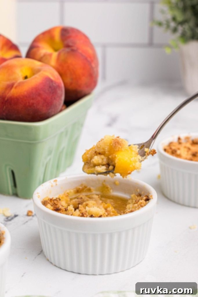 Easy Air Fryer Peach Cobbler 2 Spoonful of peach cobbler over a ramekin with peaches behind the ramekin.
