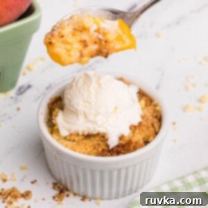 Easy Air Fryer Peach Cobbler 9 golden peach cobbler in a white ramekin with a spoonful lifted