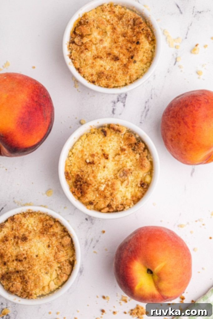 Easy Air Fryer Peach Cobbler 3 Golden peach crisps on a white marble board with fresh peaches