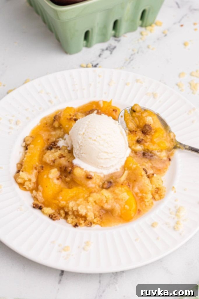 Easy Air Fryer Peach Cobbler 8 White plate with peach cobbler scooped out and topped with vanilla ice cream