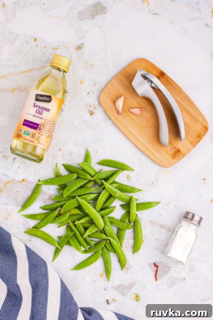 Crispy Air-Fried Snap Peas 3 Fresh snap peas, a bottle of sesame oil, minced garlic, and kosher salt arranged on a stylish marble table.