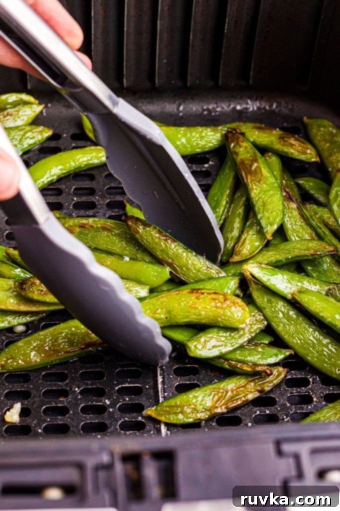 Crispy Air-Fried Snap Peas 8 Crispy air-fried snap peas being served with tongs from the air fryer basket onto a plate.