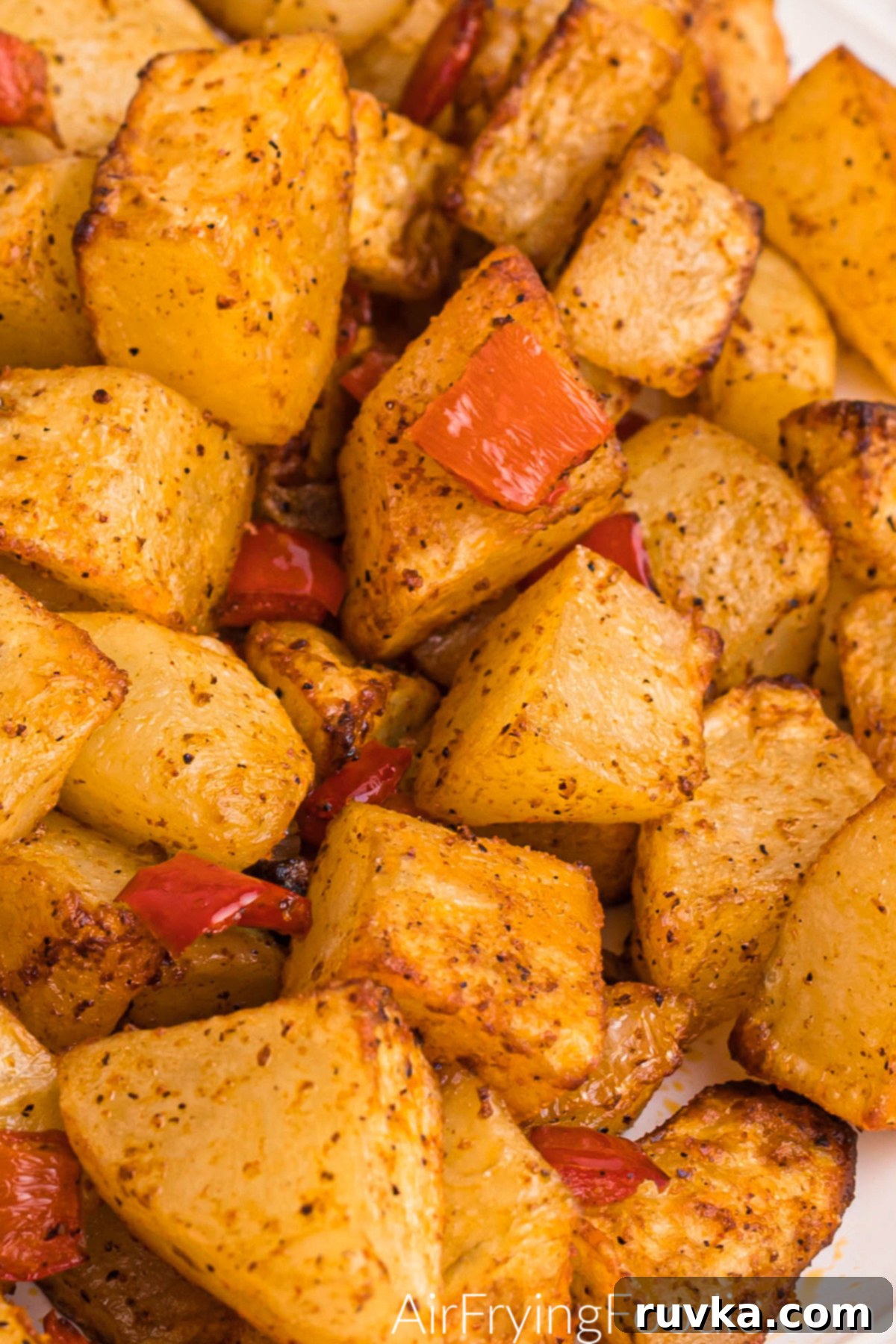 Crispy Air Fryer Home Fries 11 A white plate filled with beautifully air-fried, cubed russet potatoes, mixed with tender onion and vibrant bell pepper, ready to be served.