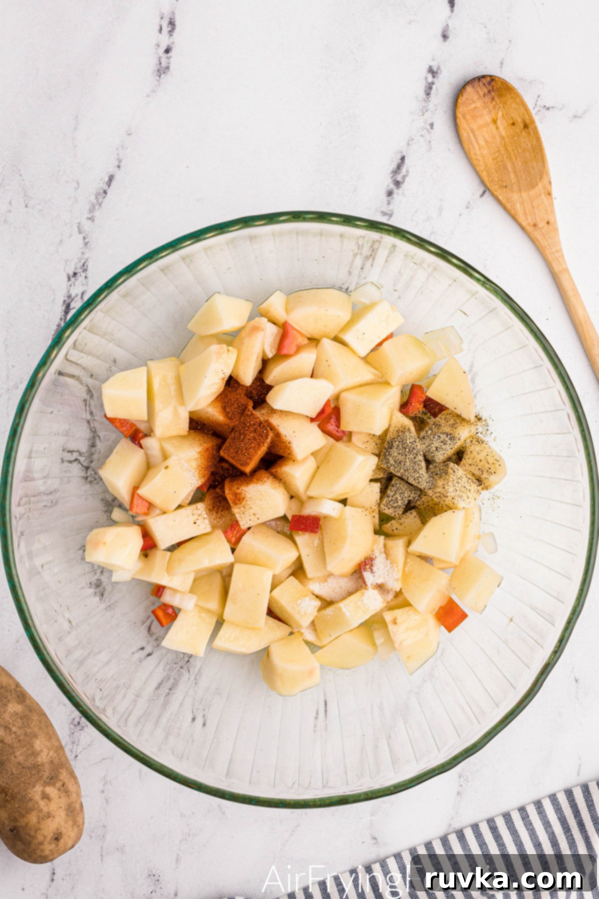 Crispy Air Fryer Home Fries 6 Seasonings added to the bowl with potatoes, bell pepper, and onion, ready to be tossed.