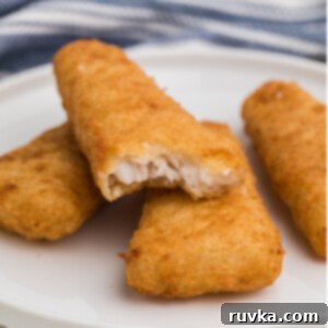 Student Air Fryer Survival Guide 9 Fully cooked frozen fish fillets made golden and crispy in the air fryer, served on a white plate with a bite missing from one.