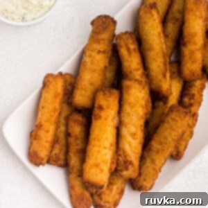 Student Air Fryer Survival Guide 10 Golden, perfectly cooked fish sticks stacked on a white plate with a side of creamy tartar sauce.