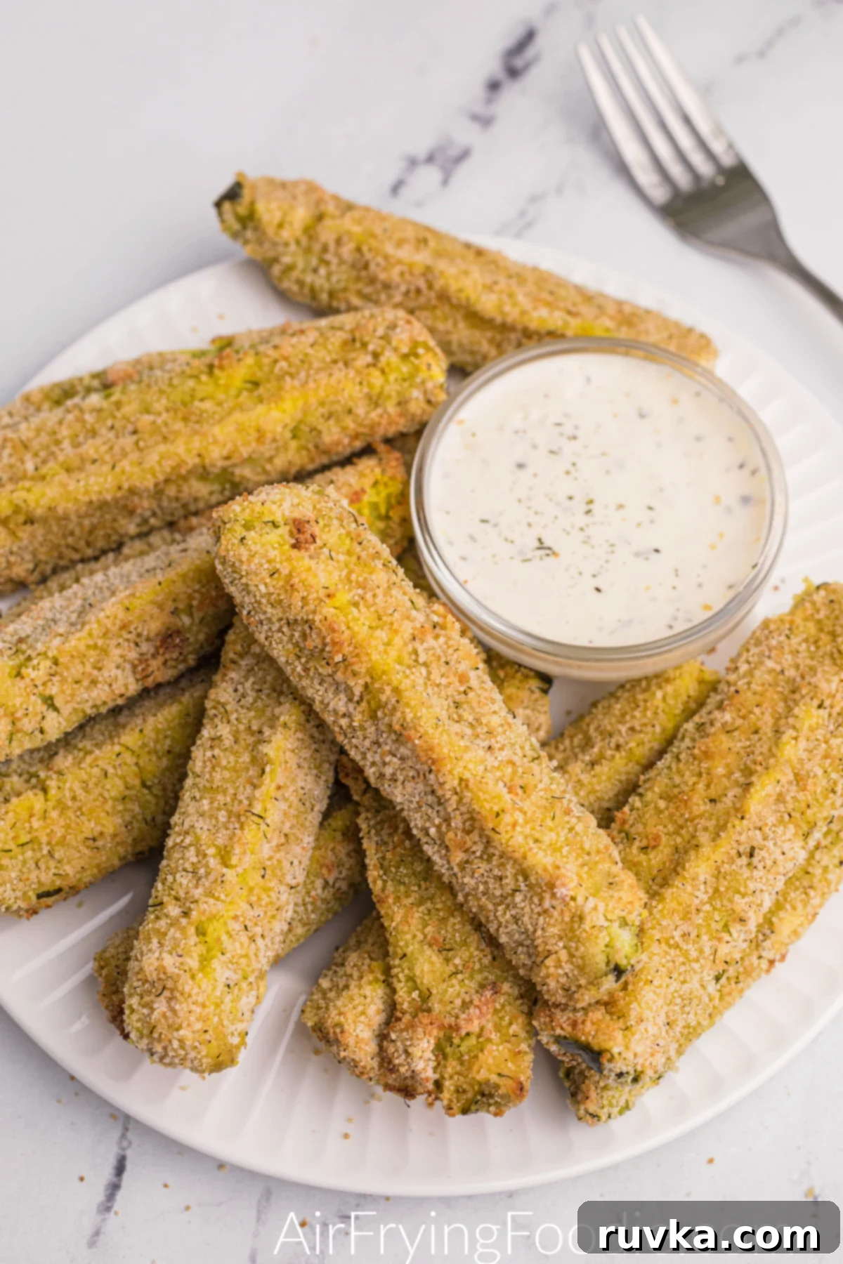 Crispy Air-Fried Dill Pickles 2 Crispy Air Fryer Dill Pickles cooked and ready to eat, served on a white plate with dipping sauce.