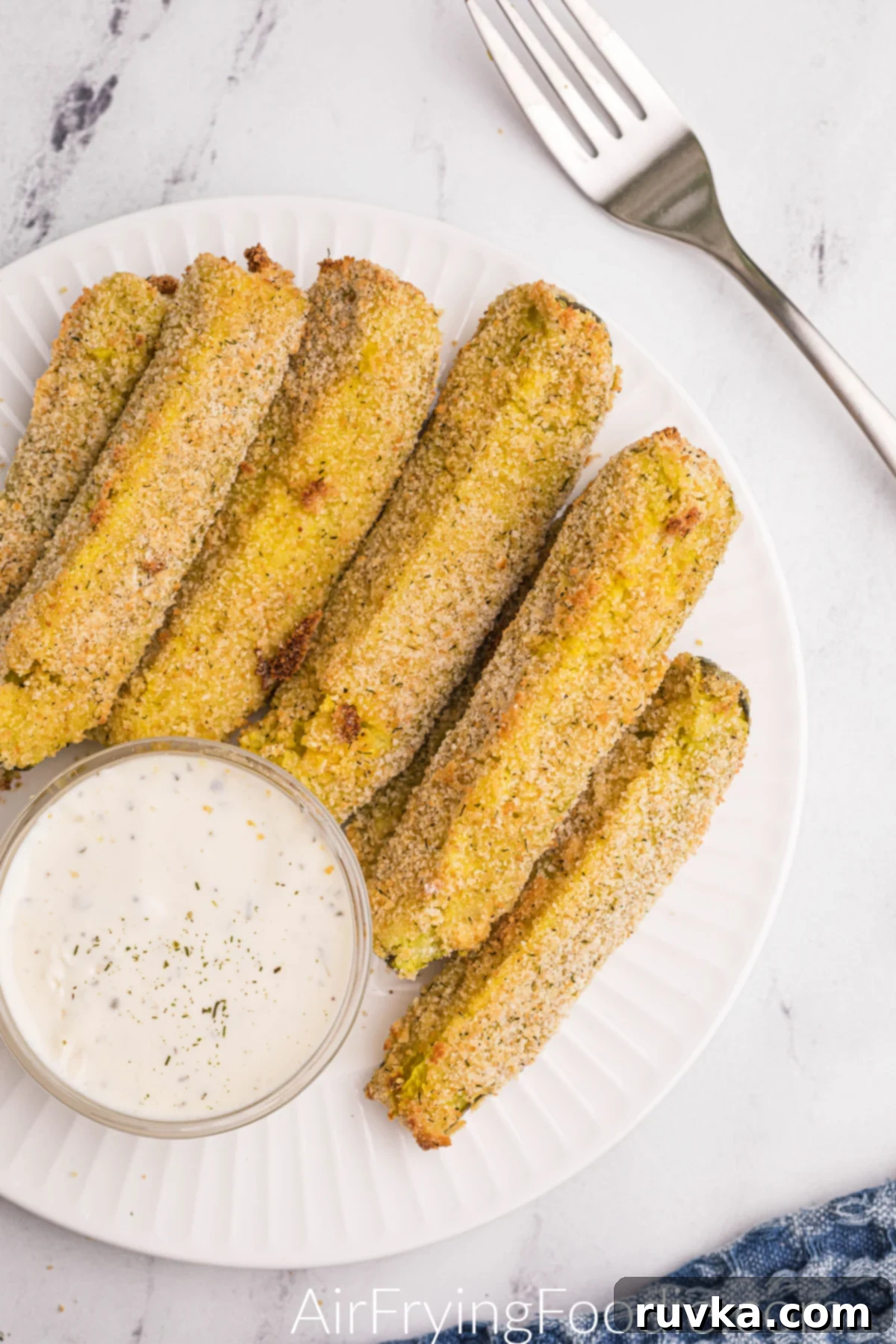Crispy Air-Fried Dill Pickles 8 Crispy golden brown air fryer dill pickle spears on a white plate with dipping sauce.
