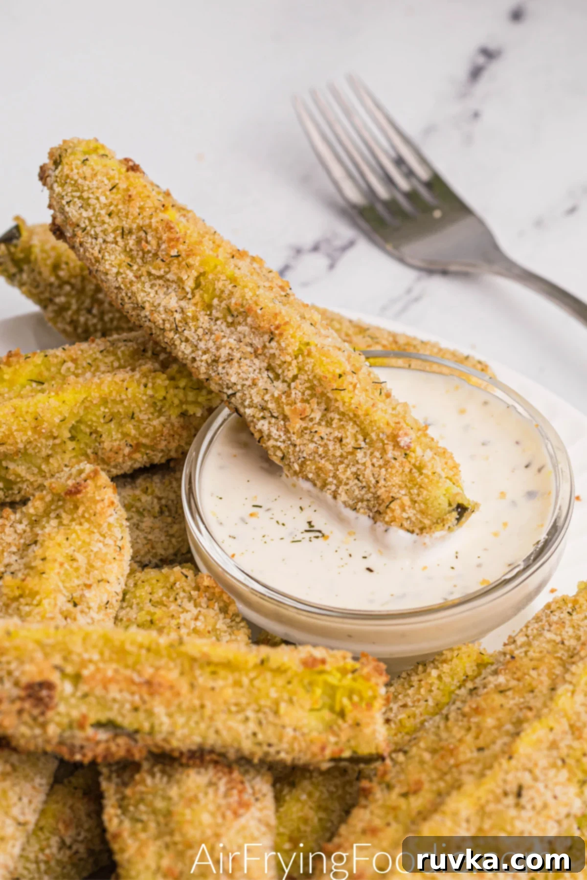 Crispy Air-Fried Dill Pickles 9 Crispy dill pickle spears on a white plate with dipping sauce.