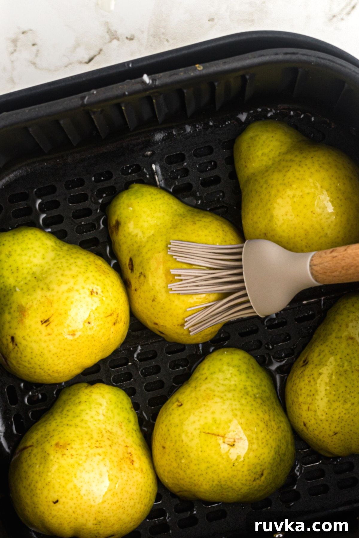Golden Air Fryer Pears 5 Brushing coconut oil on pear halves in the air fryer basket.