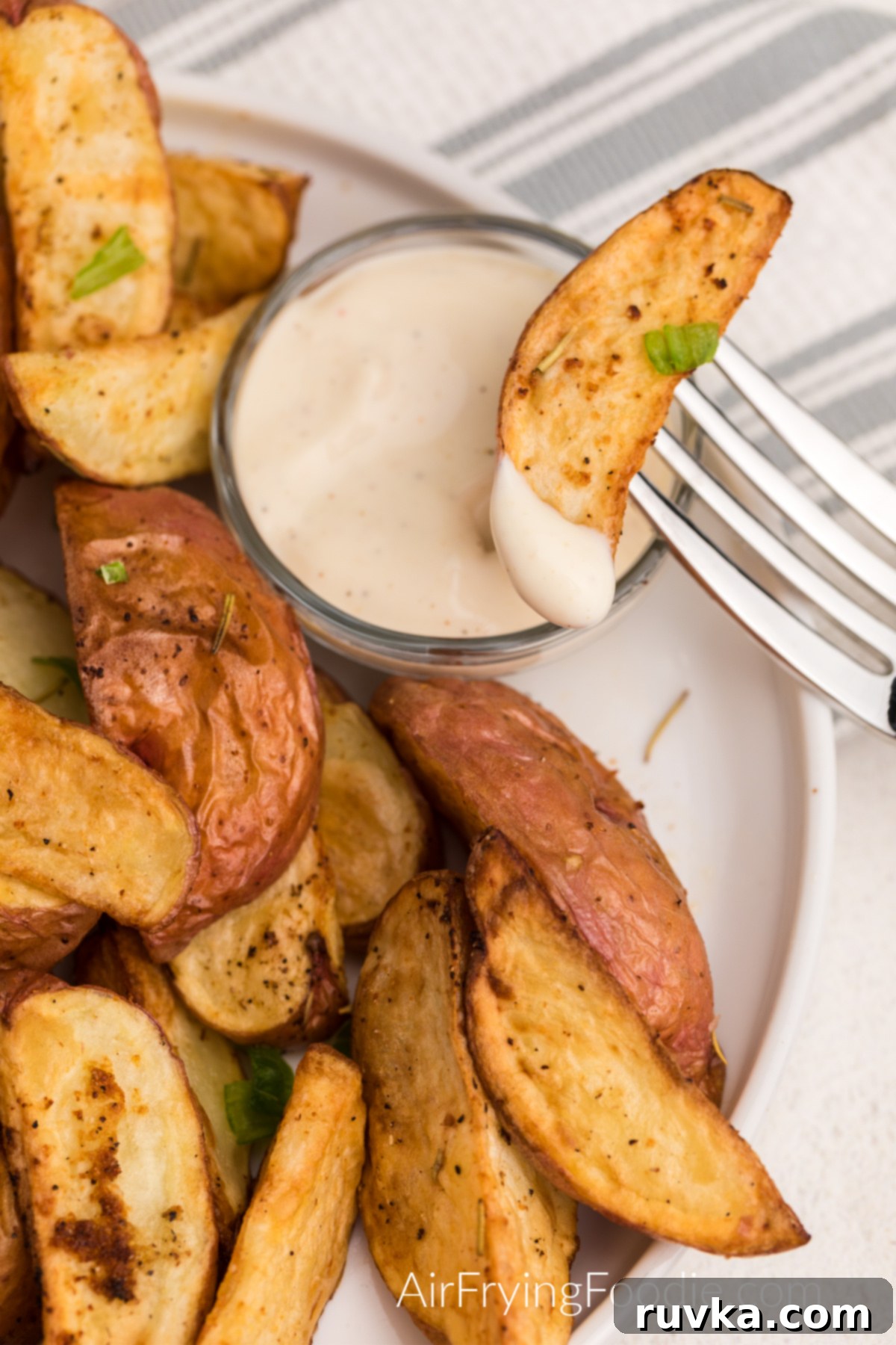 Crispy Air Fryer Red Potatoes 2 Air Fried Red Potatoes seasoned and on a white plate with dipping sauce, with one on a fork ready to eat.