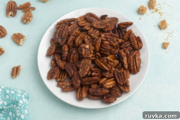 Irresistible Air Fryer Spiced Pecans 2 Spiced Pecans served on a white plate with scattered pecans and brown sugar on the table.