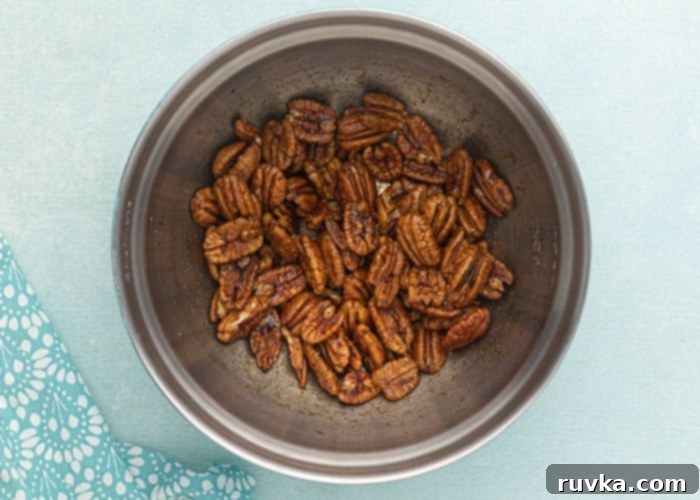 Irresistible Air Fryer Spiced Pecans 3 Pecans in a metal mixing bowl, sitting in the soy sauce and seasonings before being cooked in the air fryer.