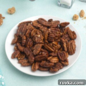 Irresistible Air Fryer Spiced Pecans 6 Cooked pecans, served on a white plate, in front of an air fryer, with scattered pecans and brown sugar around the plate.