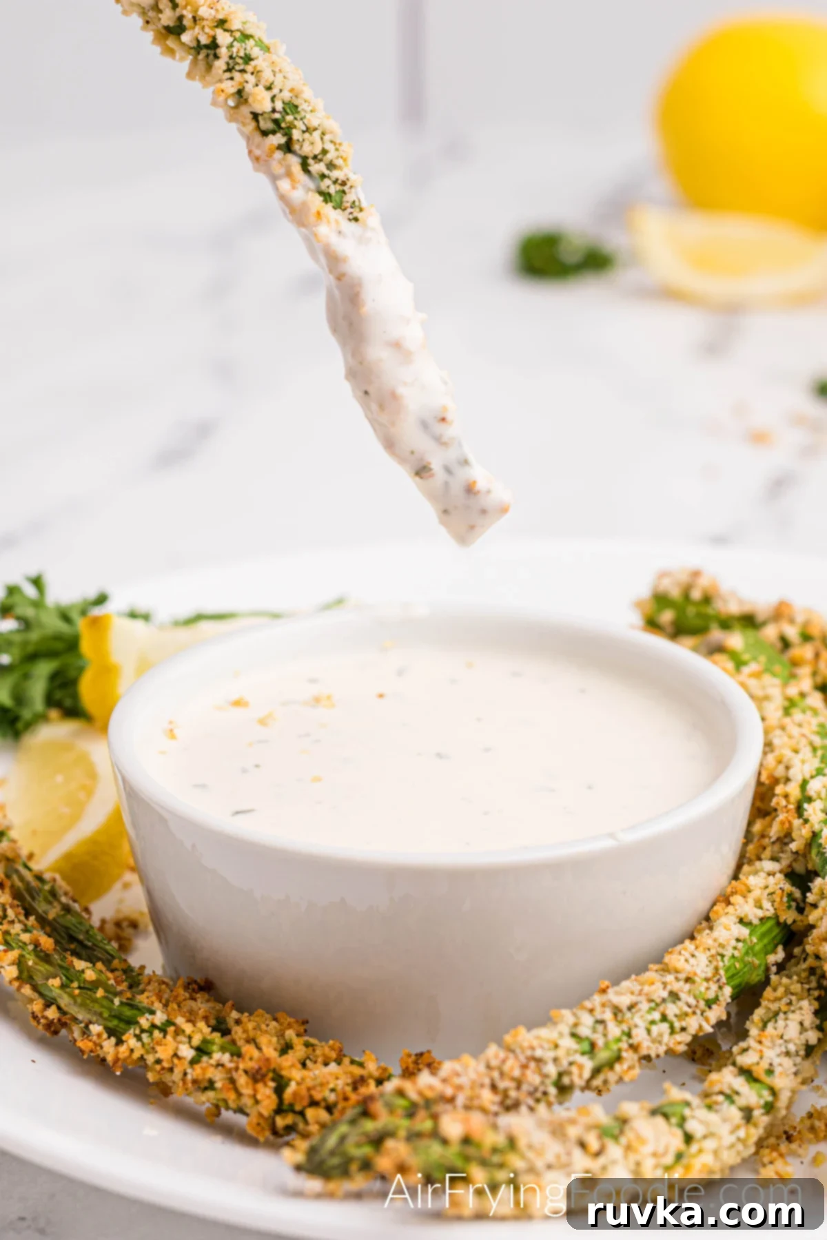 Crispy Air-Fried Asparagus Sticks 2 Asparagus fries on a white plate with one being dipped before eating.