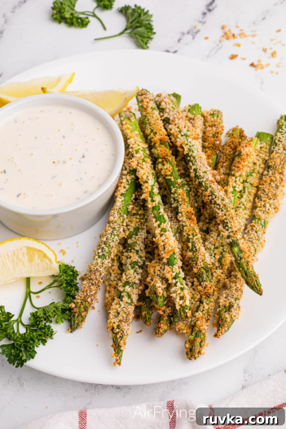 Crispy Air-Fried Asparagus Sticks 3 Air fried asparagus fries on a white plate with a lemon wedge and dipping sauce, ready to eat.