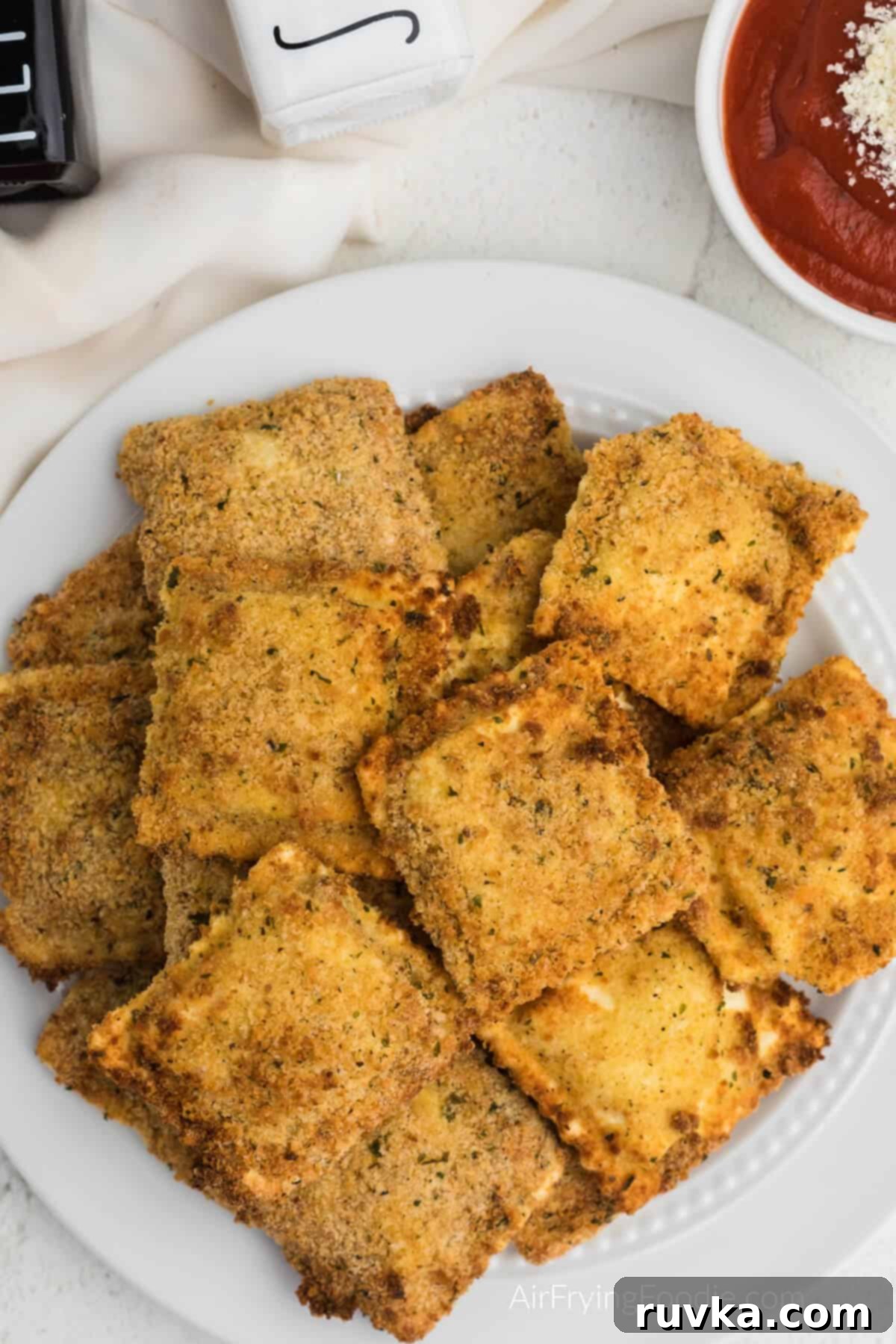 Golden Air-Fried Ravioli Bites 10 Fried ravioli made in the air fryer and served on a white plate with marinara dipping sauce.