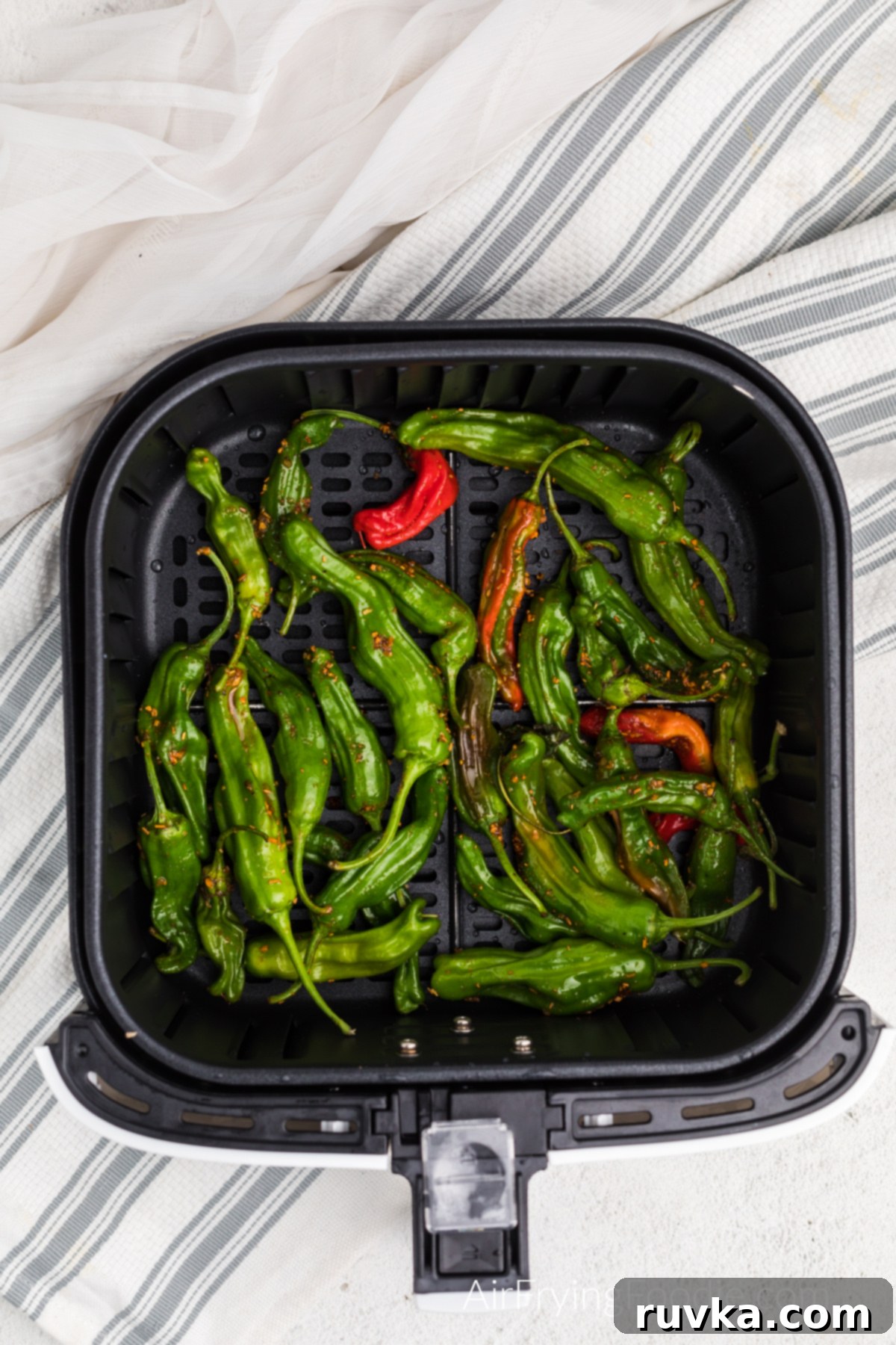 Crispy Air Fryer Shishito Peppers 4 Seasoned and oiled shishito peppers in the basket of the air fryer.