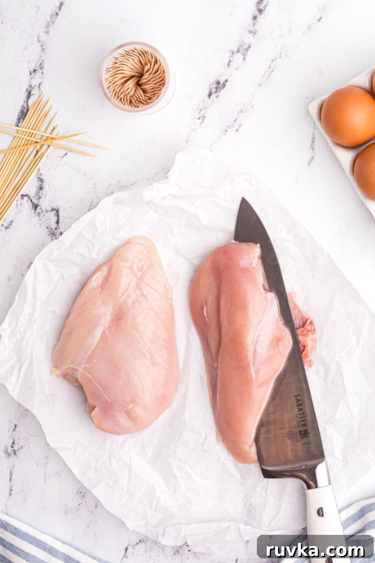 Crispy Air Fryer Chicken Cordon Bleu 4 Raw chicken breasts being sliced with a chef knife on a white marble table