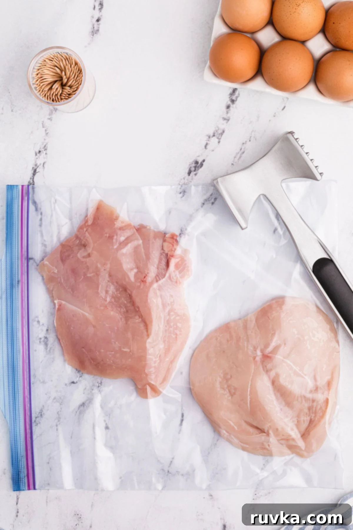 Crispy Air Fryer Chicken Cordon Bleu 5 raw chicken in a large Ziploc bag with a meat tenderizer on the table to flatten them