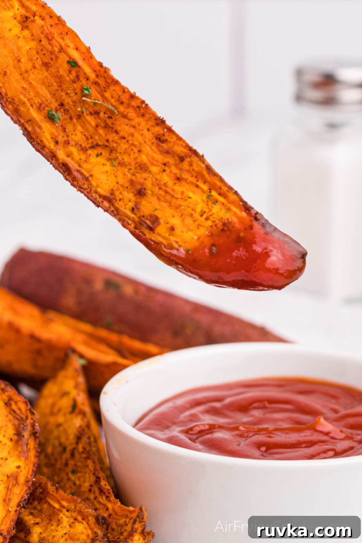 Crave-Worthy Crispy Air Fryer Sweet Potato Wedges 9 Close up of an air fried sweet potato wedge being dipped into ketchup.