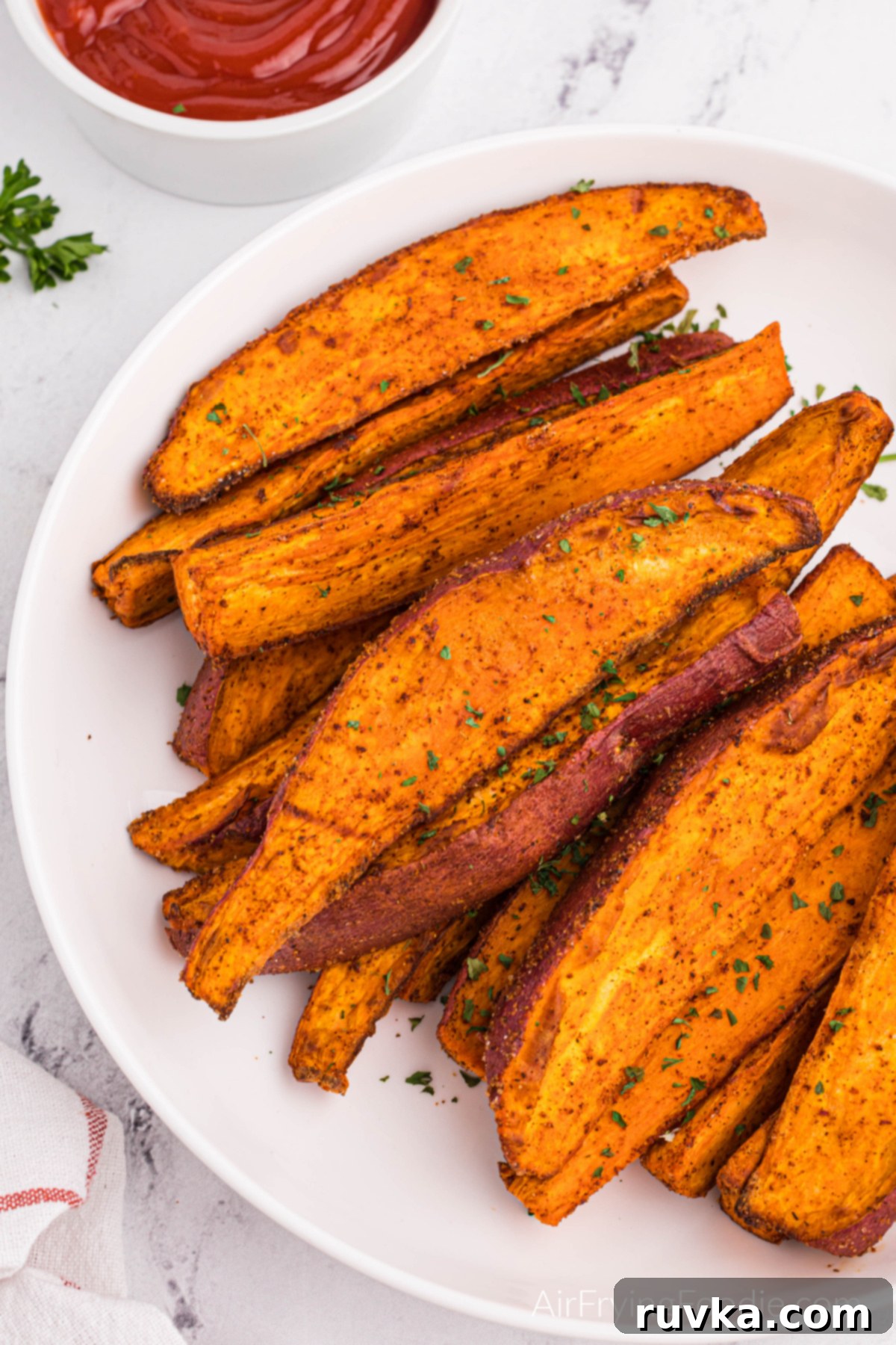 Crave-Worthy Crispy Air Fryer Sweet Potato Wedges 10 Sweet potato wedges made in the air fryer and served on a white plate with a side of ketchup.