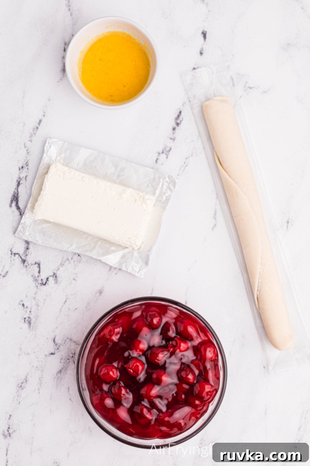 Air Fried Cherry Cream Cheese Pies 3 Essential ingredients for cream cheese cherry pies: cream cheese, a single egg, refrigerated pie crust, and a can of cherry pie filling, all laid out on a clean tabletop.