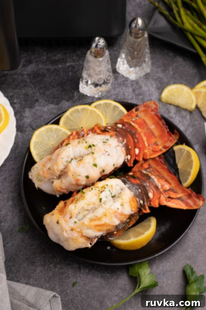 Crispy Air-Fried Lobster Tails 2 Juicy orange-red lobster tails on a black plate with lemon wedges on a black marble table. Golden, perfectly cooked lobster meat sitting atop its bright red shell, garnished with fresh lemon wedges, ready to be enjoyed.