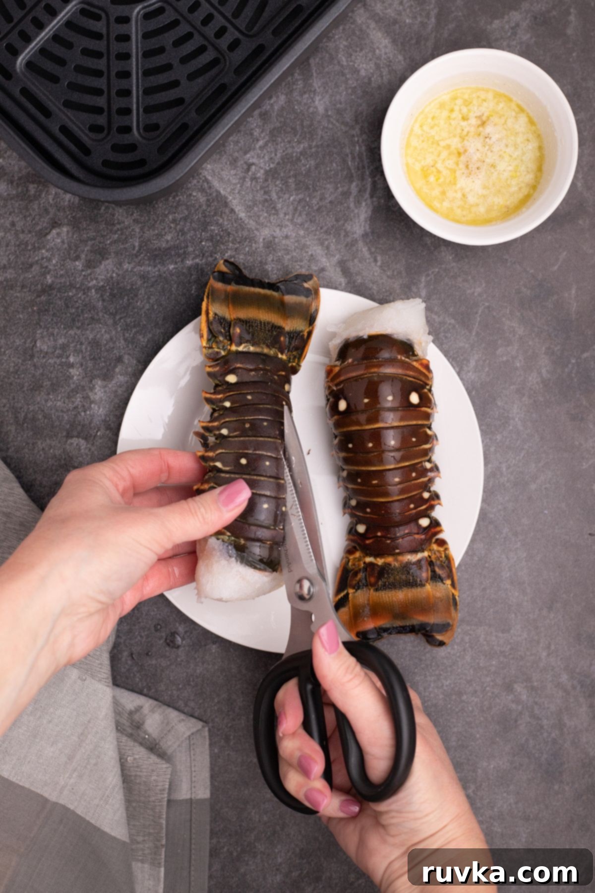 Crispy Air-Fried Lobster Tails 4 Lobster tails being cut open with kitchen shears on a white plate. A chef's hands carefully butterflying a lobster tail with sharp kitchen shears, creating a precise cut down the center of the shell.
