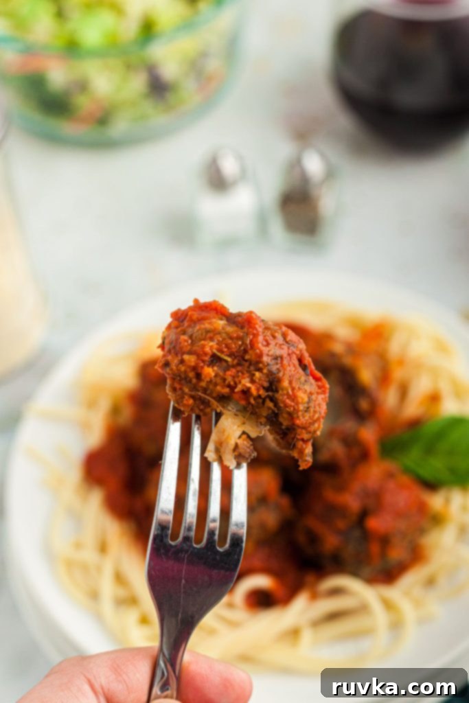 Crispy Air Fryer Cheese Stuffed Meatballs 8 Cheese filled meatball on a fork over a plate of meatballs and pasta