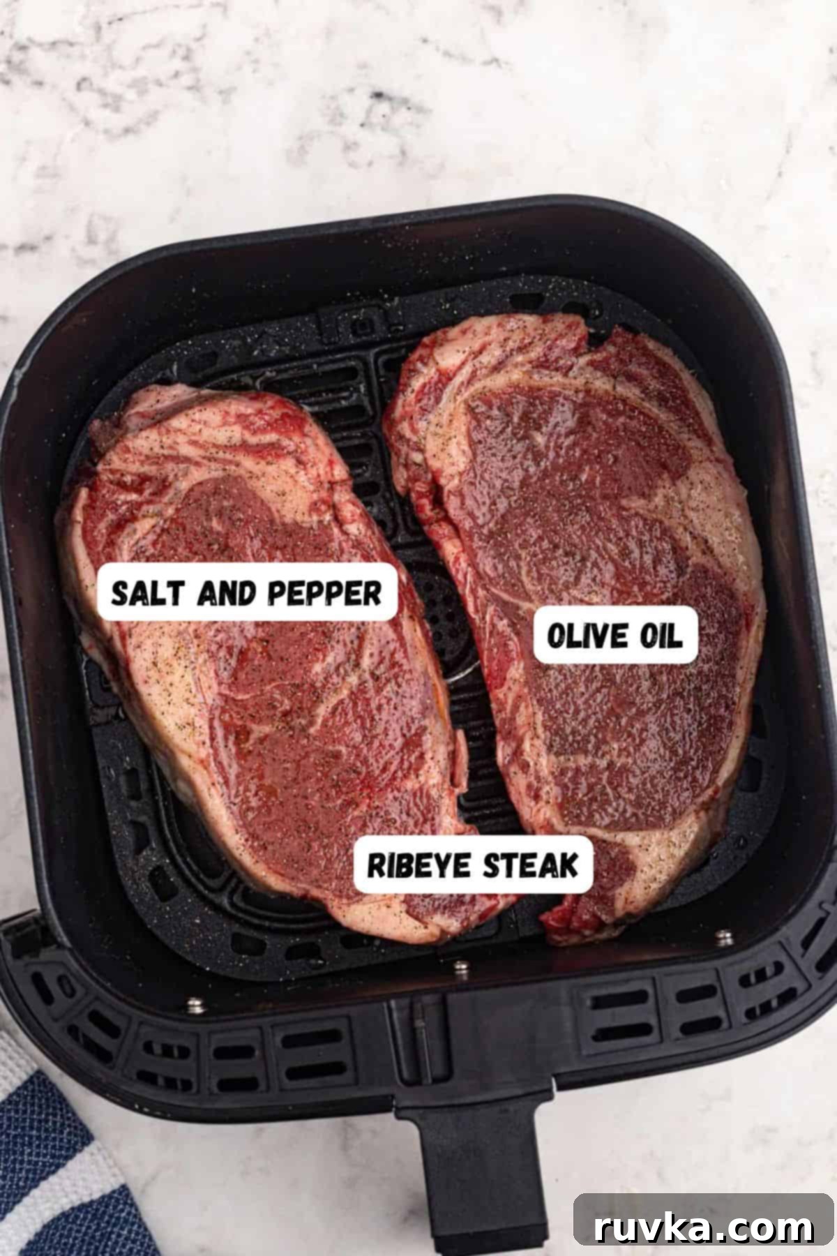 Ultimate Air Fryer Ribeye 3 Uncooked ribeye steaks in an air fryer basket with olive oil, salt, and pepper.