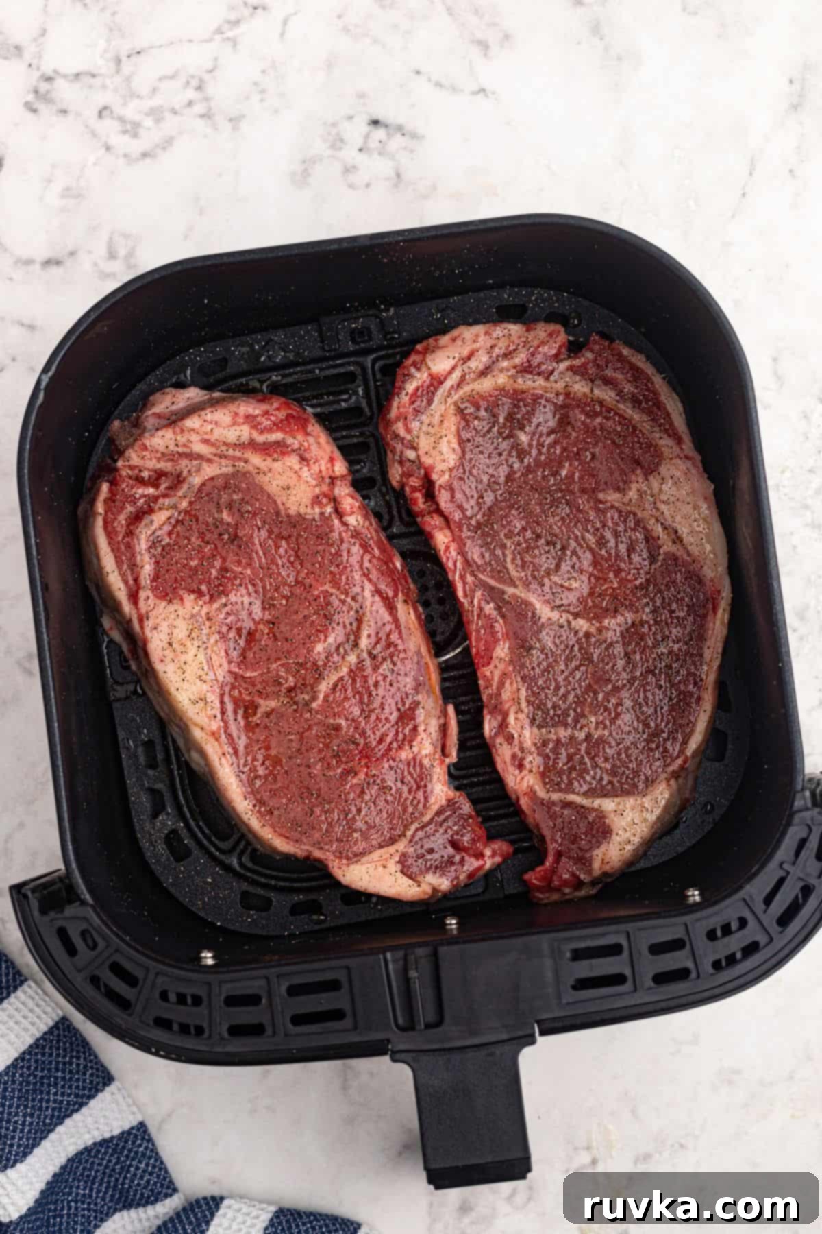 Ultimate Air Fryer Ribeye 4 Uncooked ribeye steaks that have been brushed with oil, salt, and pepper, and placed in the air fryer basket.